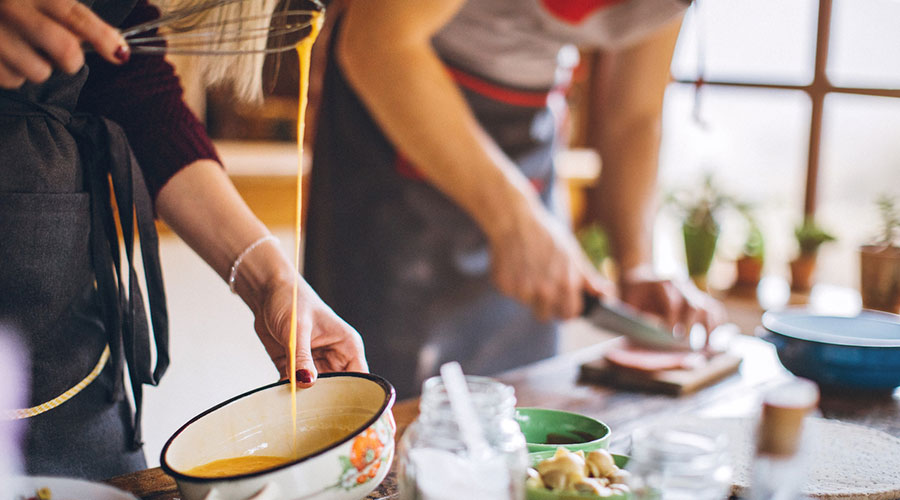 a man chopping food on a small cutting board while a woman beats eggs in a bowl.